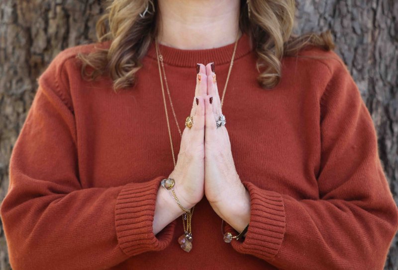 Hands in prayer position resting against a rust sweater