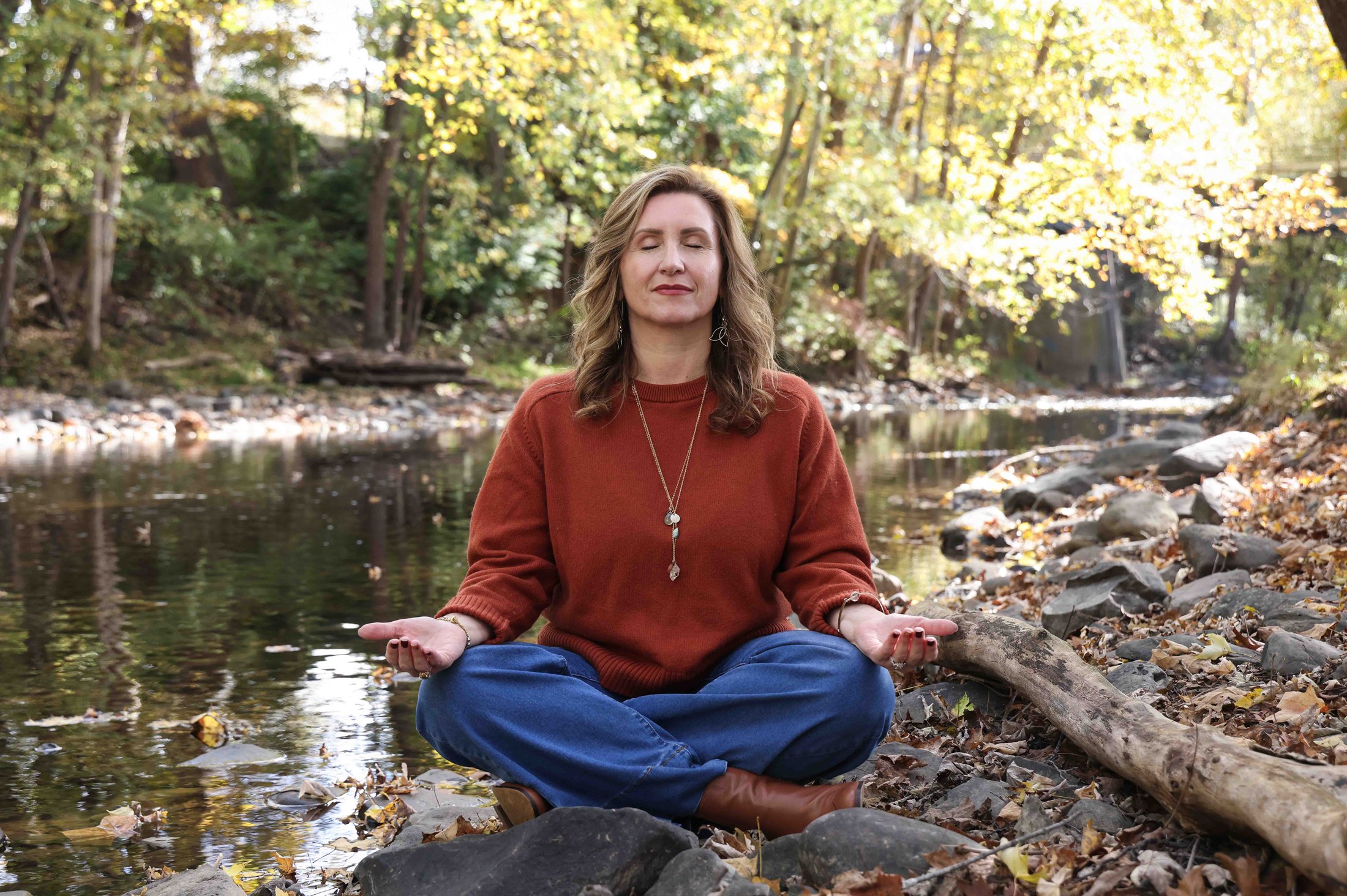 Christine Dorsey meditating beside a creek in autumn